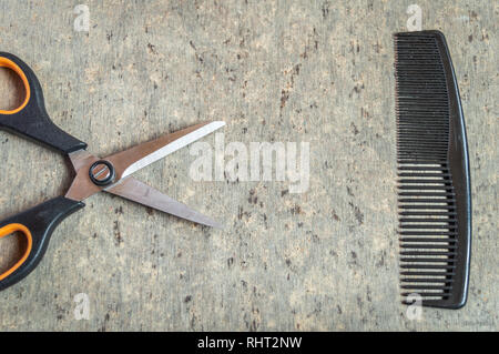 A scissors and a comb kept on a grey wooden textured table top view Stock Photo