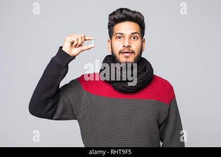 Portrait of a arabic man dressed in sweater and scarf showing pill capsule standing over gray background Stock Photo