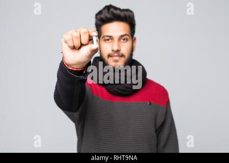 Portrait of a arabic man dressed in sweater and scarf showing pill capsule standing over gray background Stock Photo