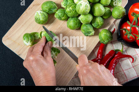 a close-up of woman's hands cutting Brussels sprouts on wooden plank Stock Photo