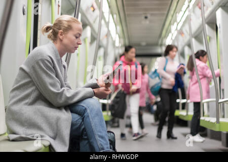 Beautiful blonde woman using smart phone while traveling by metro public transport. Stock Photo