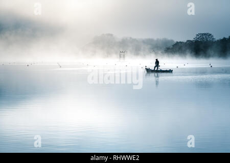 the silhouette of a fisher man with his boat on a misty moring at Lake Shoji Stock Photo