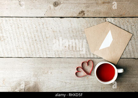 Cup of tea with red heart and craft paper envelope on vintage wooden background close up. Valentines day. Good warmong morning concept, copy space, to Stock Photo