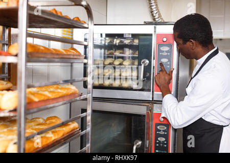 Experienced baker controlling process of baking bread, programming professional oven at bakery Stock Photo