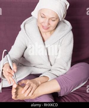 Elderly woman performing pedicure with special devices at home Stock Photo