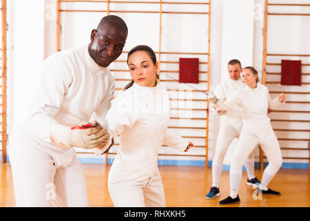 Female fencer practicing  movements with african american male trainer at workout Stock Photo