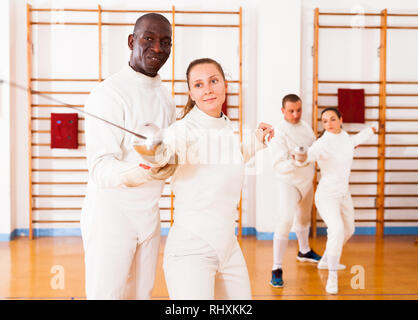 Female fencer practicing  movements with african american male trainer at workout Stock Photo