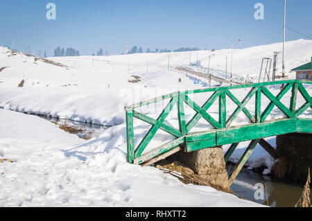 A green colour small wooden bridge over an small stream river in a snow landscape Stock Photo