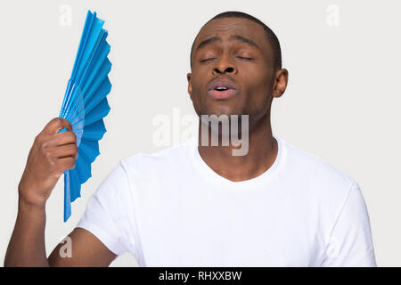 African man suffering from heat using fan isolated on background Stock Photo