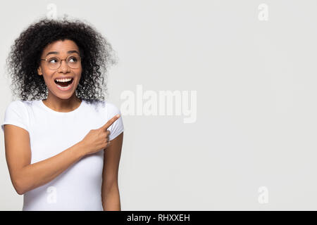 Excited african woman looking up aside pointing finger at copyspace Stock Photo