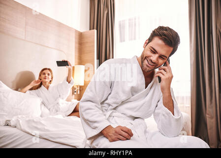 Connection with relatives. Couple are using smartphones in hotel room bed. Technologies win Stock Photo