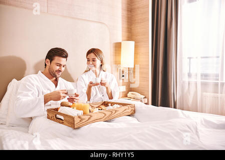Food delivery in the room. Couple are eating in hotel room bed together. Love story. Waiter bring breakfast to couple Stock Photo