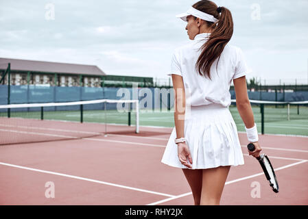 Beautiful girl in white polo and skirt with the racket in her hand is going to play tennis on the court Stock Photo