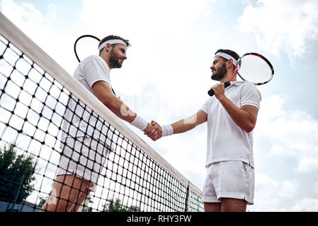 Two handsome tennis players shake hands on the court after the match Stock Photo