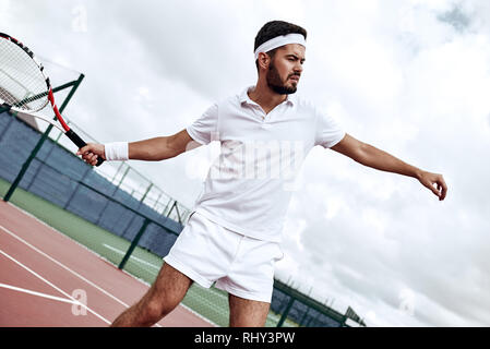 Handsome man in white polo is ready to let the ball bounce standing on the court Stock Photo