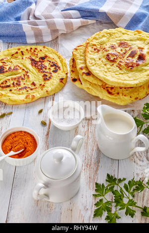 naan - delicious hot freshly baked indian flatbread on a white table with ingredients and stack of flatbreads at the background, vertical view from ab Stock Photo