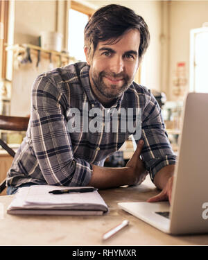 Young entrepreneur using a laptop in his workshop Stock Photo