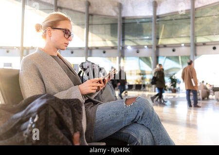 Female traveler using her cell phone while waiting to board a plane at departure gates at airport terminal. Stock Photo