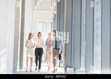Professionals communicating while walking in office corridor Stock Photo