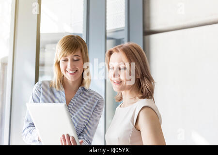 Professionals discussing over digital tablet in office corridor Stock Photo