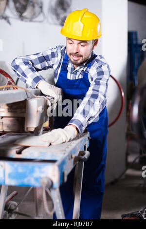 Male is using disk saw to cut tile at workshop. Stock Photo