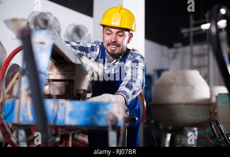 Adult worker is using disk saw to cut tile at workshop. Stock Photo
