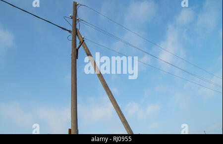 Wooden old 0.4 kV power line support with wires and insulators on blue sky background Stock Photo