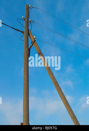 Old wooden support of power transmission lines 0.4 kV with wires and insulators on a blue sky background, vertical image Stock Photo