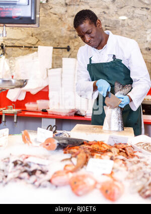 African American seller preparing raw fish for customers at seafood market Stock Photo