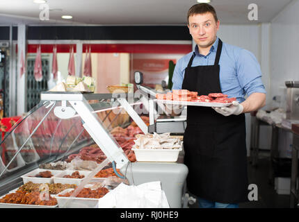 Professional butcher arranging meat products in display case of butcher shop Stock Photo