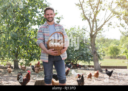 Man holding eggs in basket with chickens in background at farm Stock Photo