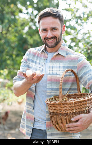 Portrait of smiling farmer holding eggs in basket at farm Stock Photo