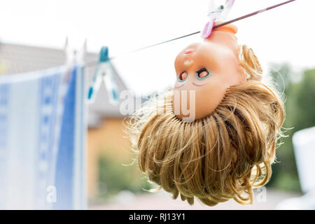 Closeup of abandoned broken doll head hanging on clothesline Stock Photo