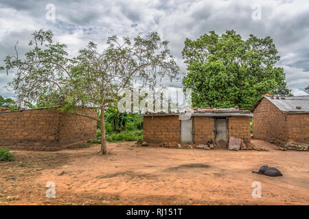 View of traditional village, a coat resting outdoor and zinc sheet on roof houses and terracotta brick walls, cloudy sky as background, in Angola Stock Photo