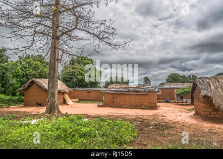 View of traditional village, thatched and zinc sheet on roof houses and terracotta brick walls, cloudy sky as background, in Angola Stock Photo