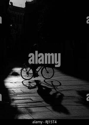 Strong Graphic Shadow Silhouettes of cyclists on bikes in pool of sunlight on street Seville Spain Stock Photo