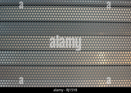 Metal plate with circular holes over parallel horizontal metal blinds background texture. Stock Photo