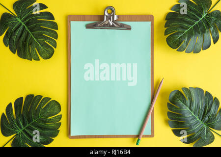 Flat lay of blank clip board and monstera leaves against yellow background minimal summer creative concept. Space for copy. Stock Photo