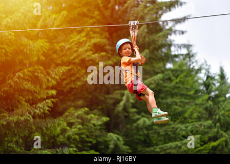 Happy kid with helmet and harness on zip line between trees Stock Photo