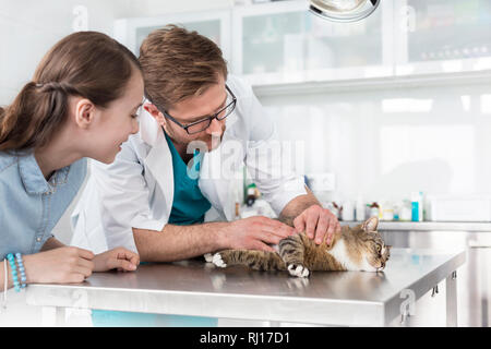 Doctor examining cat on table by girl in veterinary clinic