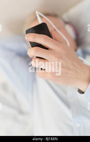 High angle view of man using smartphone while lying on bed Stock Photo