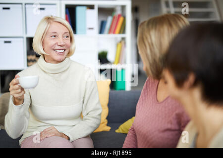 Portrait of smiling mature woman talking to friends drinking tea during break in office, copy space Stock Photo