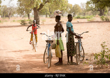 Samba village, Yako Province, Burkina Faso; schoolgirls on their way home from school wait in the shade for a friend. Stock Photo