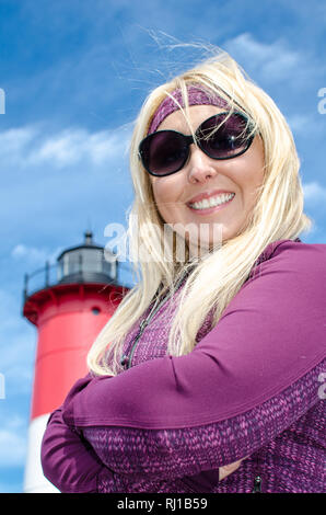 Portrait of a beautiful blonde woman, smiling with her arms crossed in front of Nauset Lighthouse on Cape Cod Stock Photo