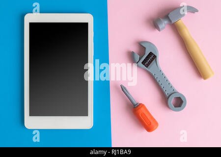 Digital tablet device or mobile phone with hammer, wrench and screwdriver on pastel background minimal technology repair creative concept. Stock Photo