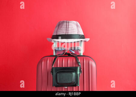 Suitcase with hat and retro camera on red background. Travel equipment minimal creative concept. Stock Photo