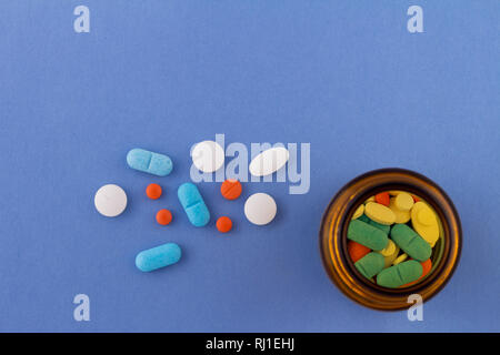 Colored pills on a light blue background next to a glass bottle containing drugs. Drugs for use in humans. Stock Photo