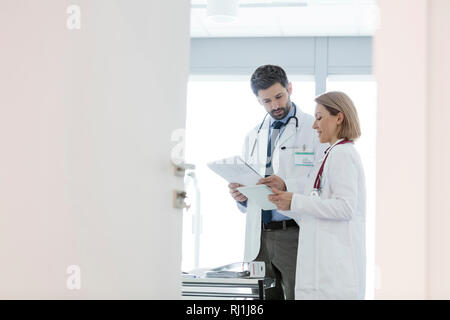 Colleagues discussing over medical records at desk seen through open door in hospital Stock Photo