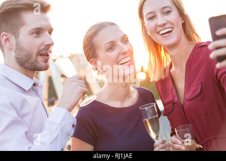 Smiling young businesswoman taking selfie with colleagues during rooftop party Stock Photo