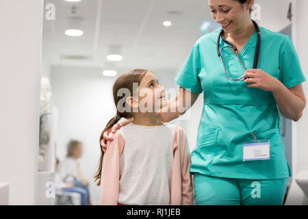 Smiling girl looking at mid adult nurse while walking in hospital corridor Stock Photo